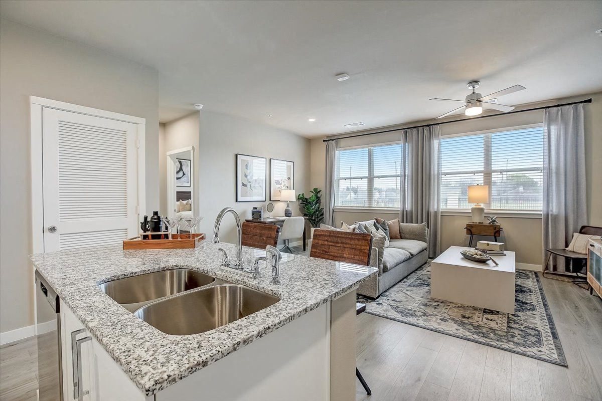 Kitchen overlooks airy living and dining area with neutral furnishings and wide windows.